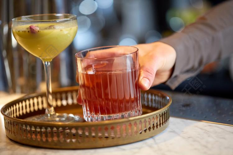 酒精饮料,人们和豪华概念-把杯鸡尾酒放的酒保放盘子在酒吧酒保戴着